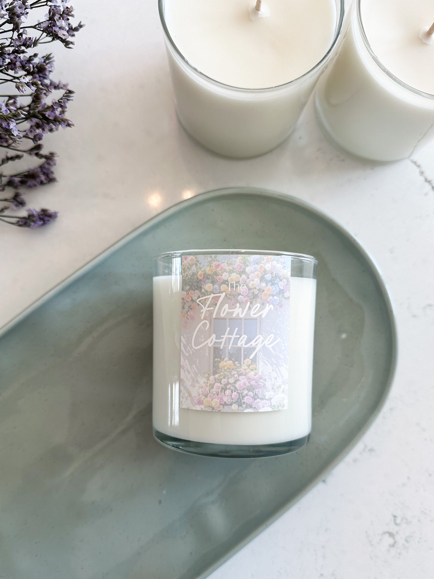 Candle with 'Flower Cottage' label on a gray tray with lavender flowers.