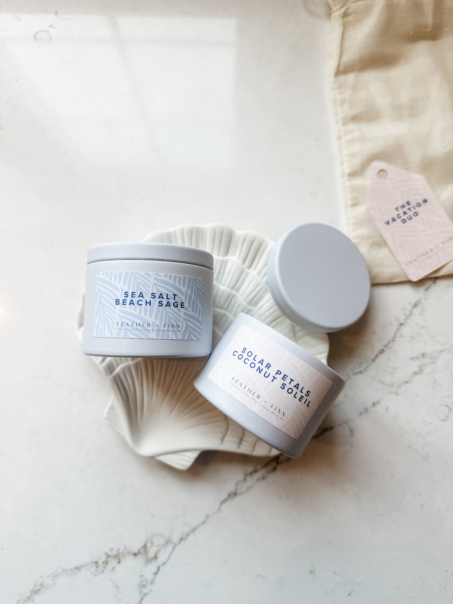 Two containers of sea salt and coconut soaps on a marble surface with a white background.