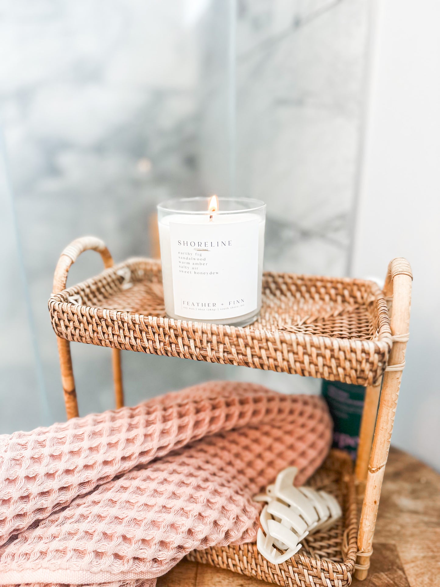 Candle on a wicker shelf with a pink blanket and white decor item in the background