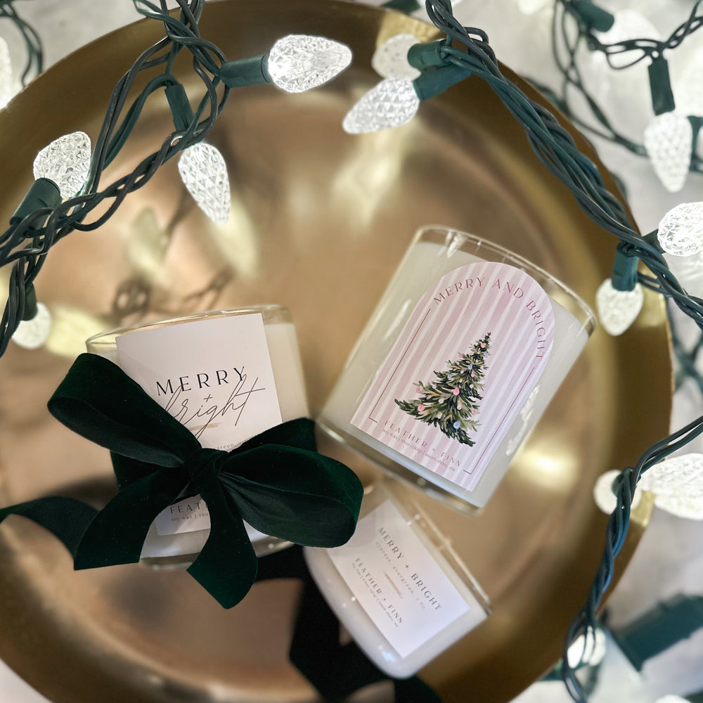 Three candles labeled merry + bright in a gold dish with twinkle lights.