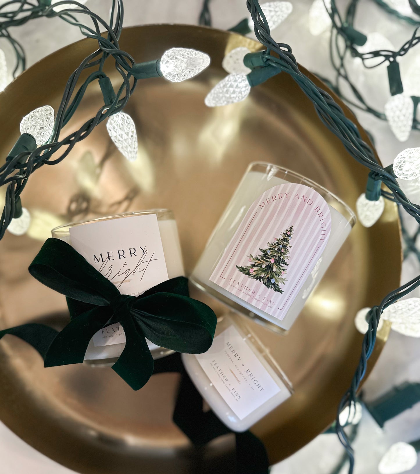 Three candles labeled merry + bright in a gold dish with twinkle lights.