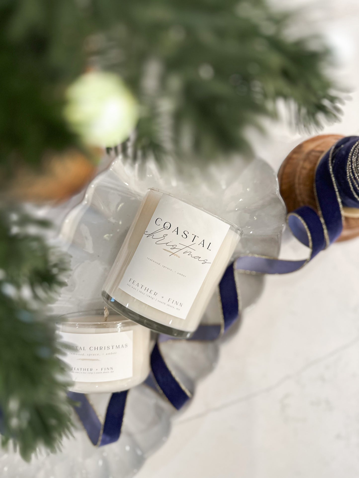 Candle labeled 'Coastal Christmas' with a blue ribbon under a Christmas tree.